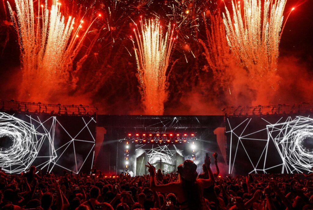 Vibrant festival concert scene with fireworks lighting up the night sky and a lively audience.