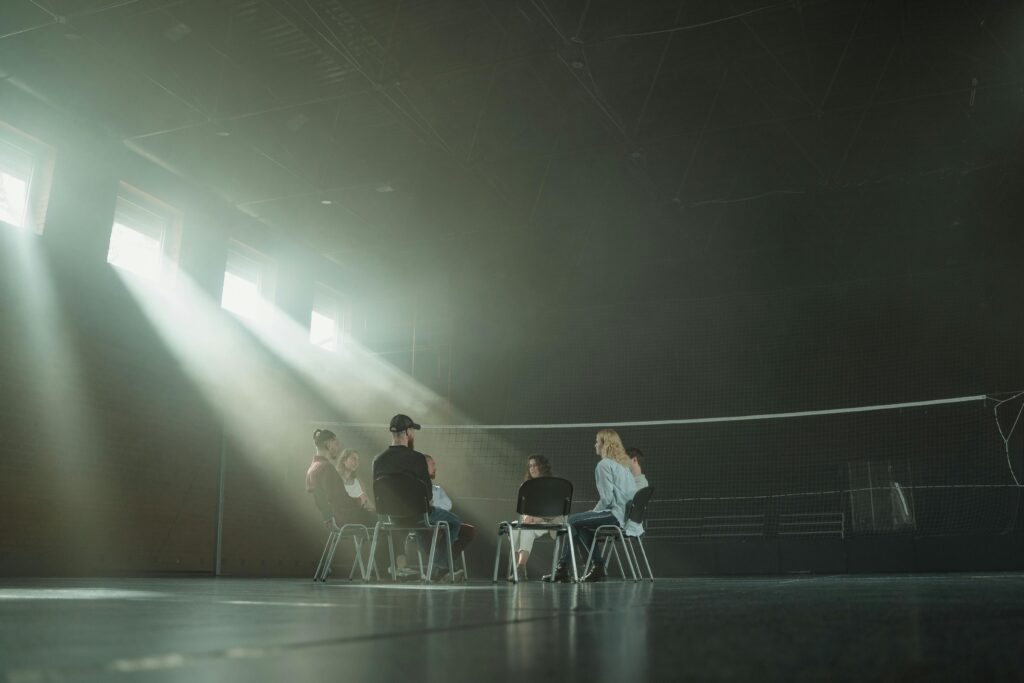 A small group of people participating in a support session, illuminated by sunrays in a spacious hall.